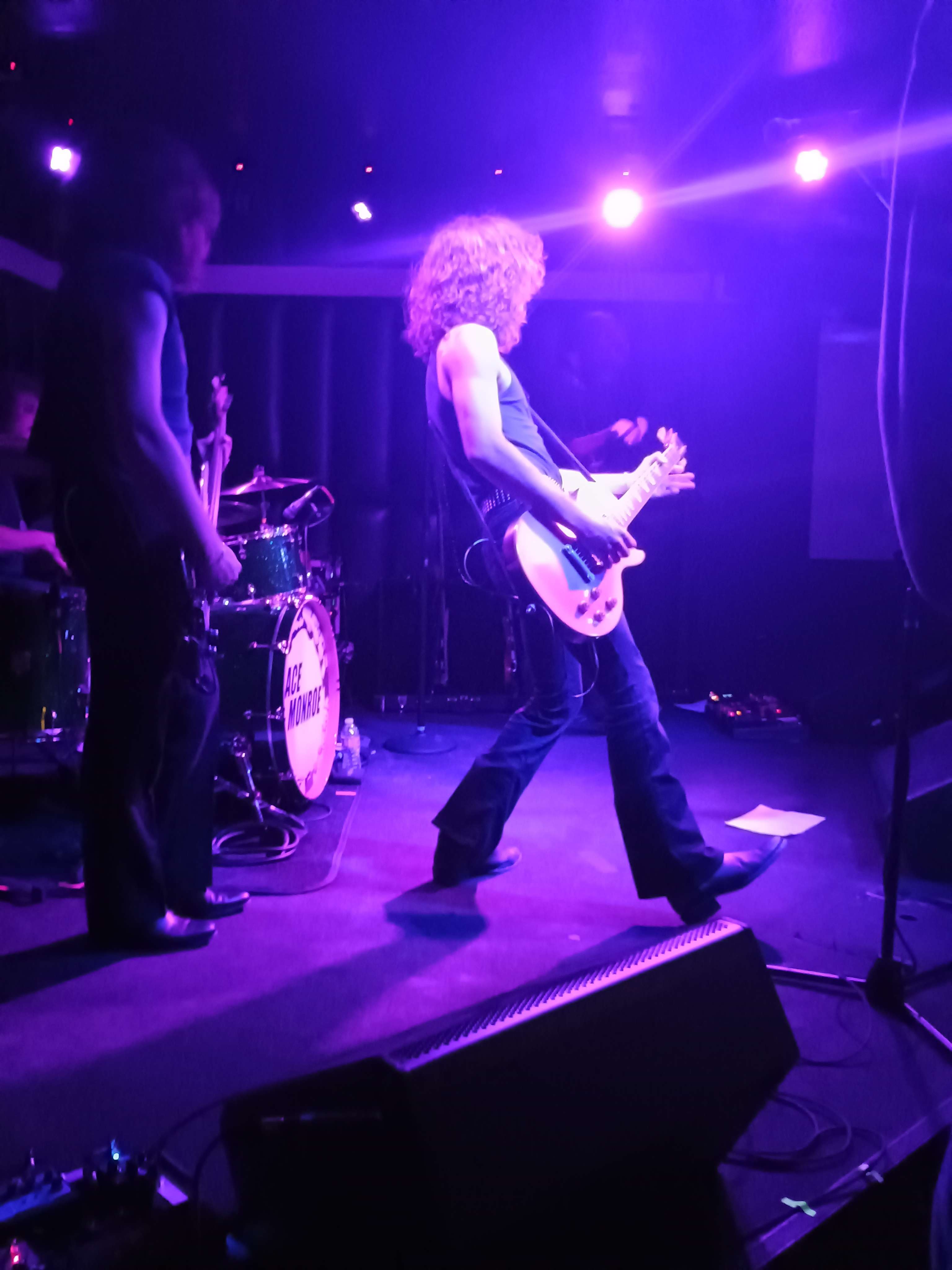 A man plays bass guitar on a stage lit by blue lights.