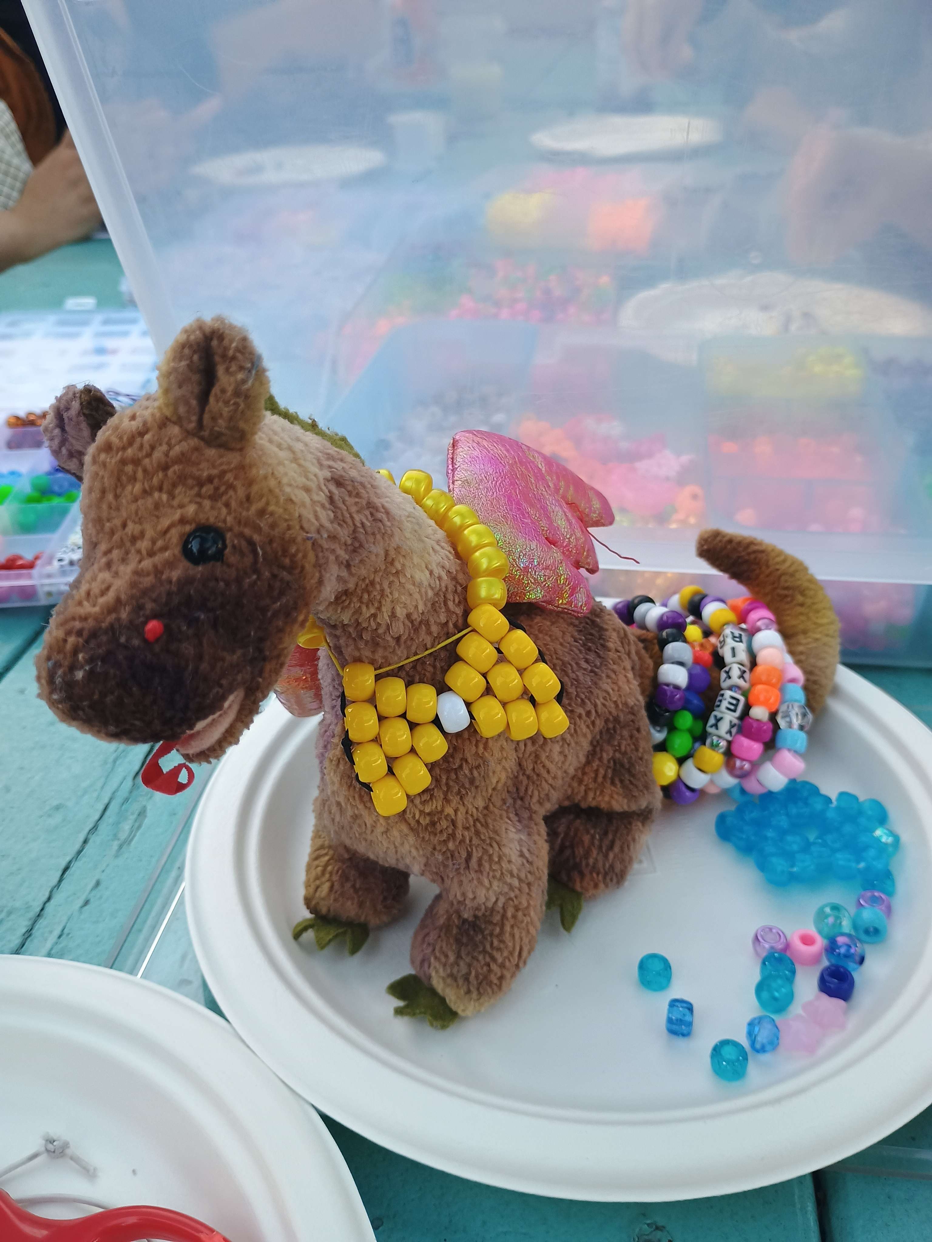 A plush dragon wearing a bead bowtie sits on a plate.
